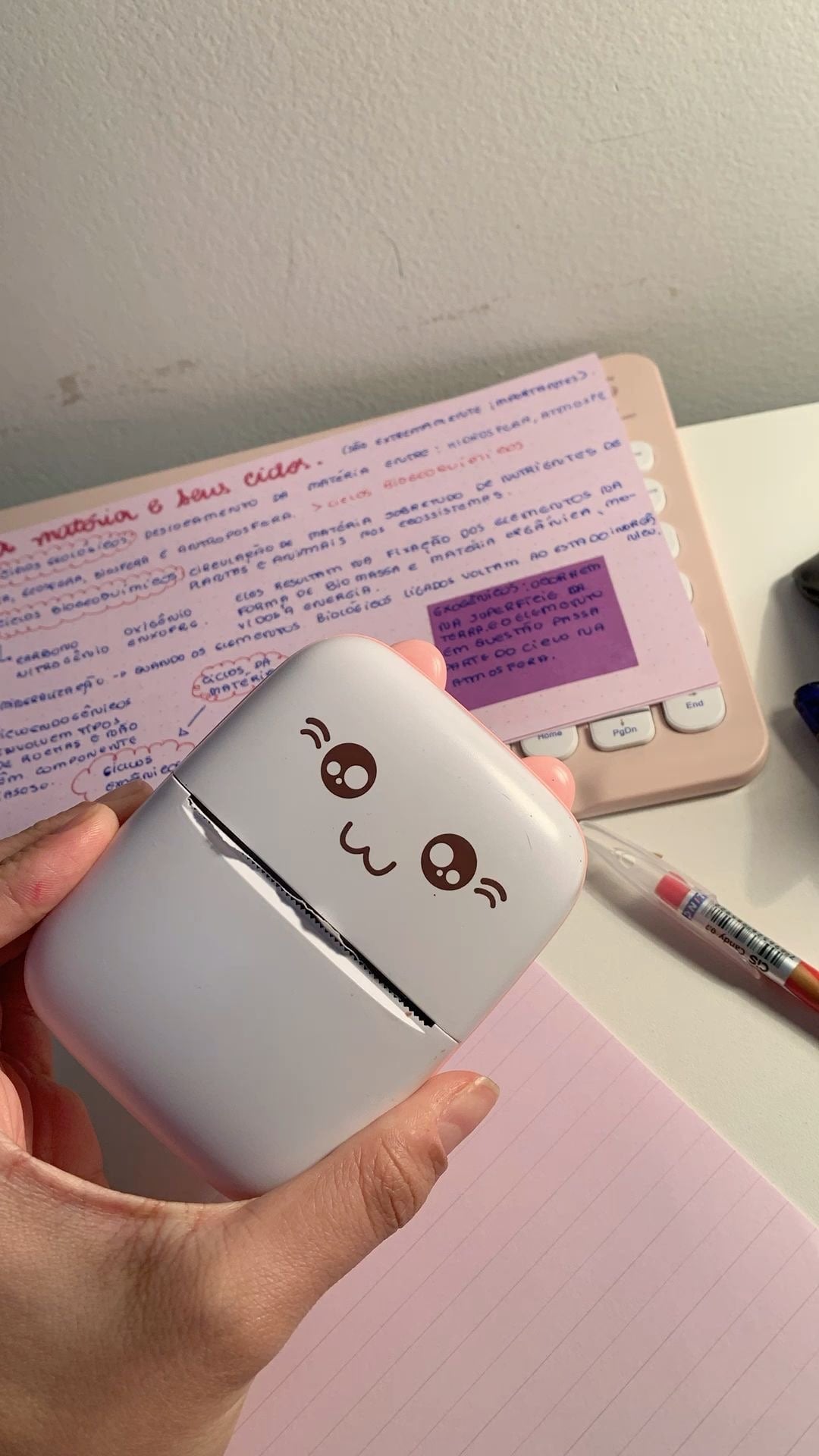 La mini imprimante Imprimini rose tenue dans la main, sur un bureau avec des fiches de révision